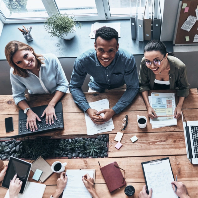 A diverse team collaboratively working around a table with documents, laptops, and digital devices, representing the company's mission of teamwork and quality service.